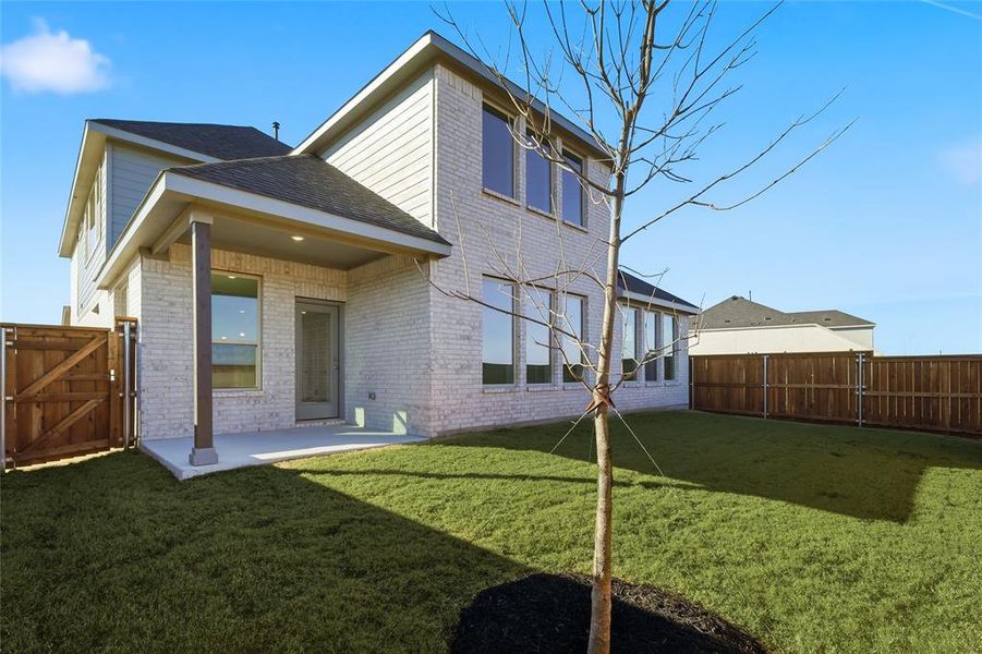 Rear exterior featuring light-colored brick and siding, a covered patio with a concrete slab, a wood privacy fence, and a grass lawn