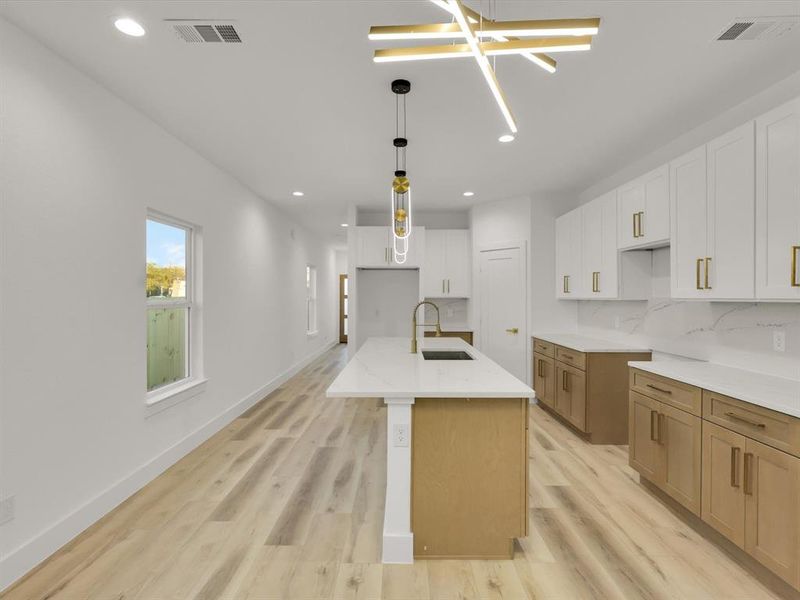 Kitchen with white cabinetry, a kitchen island with sink, sink, and light wood-type flooring