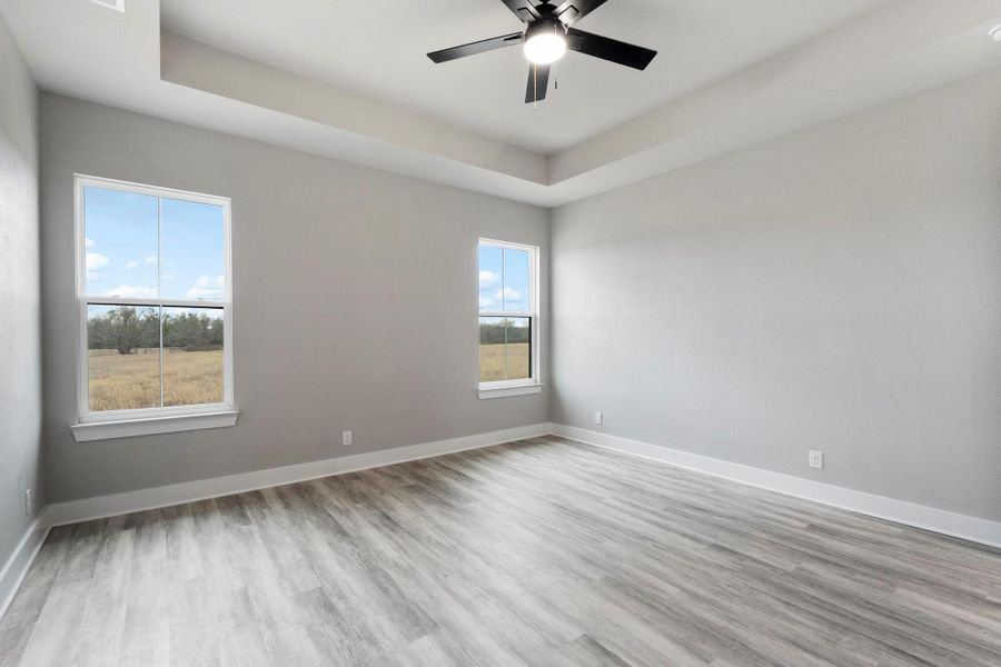 Spare room with a tray ceiling, light wood-style flooring, and ceiling fan