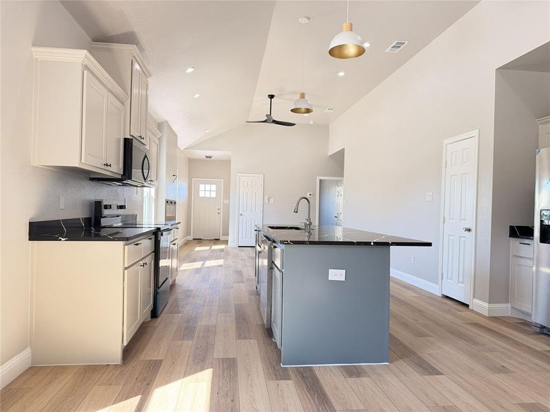 Kitchen with stainless steel appliances, vaulted ceiling, an island with sink, ceiling fan, and light wood-type flooring