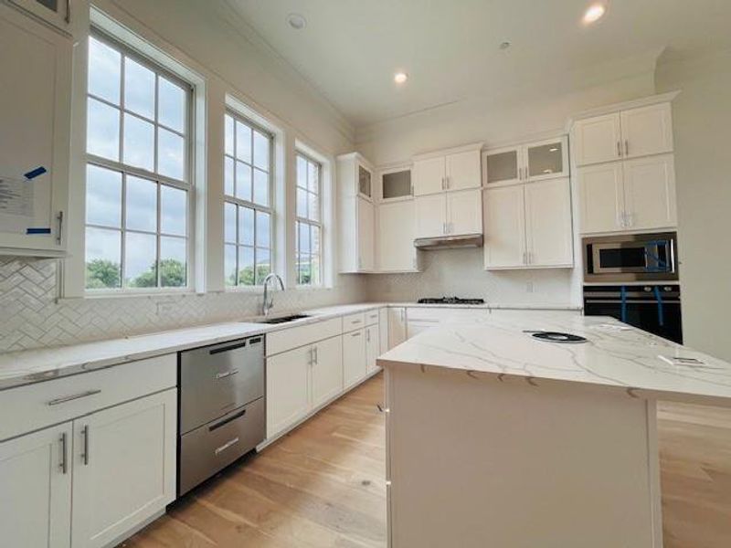 Kitchen featuring glass insert cabinets, light stone countertops, light wood-style flooring, ornamental molding, and a kitchen island