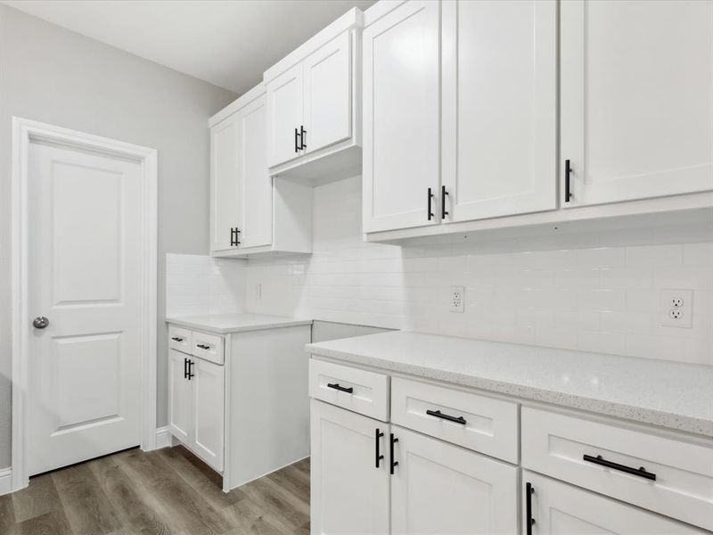 Kitchen featuring light stone counters, tasteful backsplash, white cabinets, and hardwood / wood-style flooring