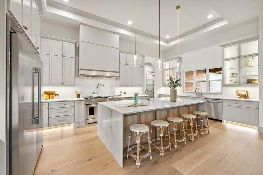 Kitchen featuring light stone counters, decorative backsplash, high quality appliances, a breakfast bar, and light wood-style flooring Kitchen featuring light stone counters, decorative backsplash, high quality appliances, a breakfast bar, and light wood-style flooring