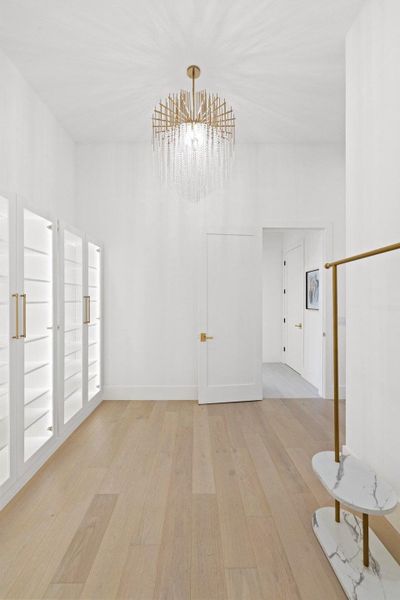 A refined walk-in closet with illuminated built-ins and natural wood flooring.