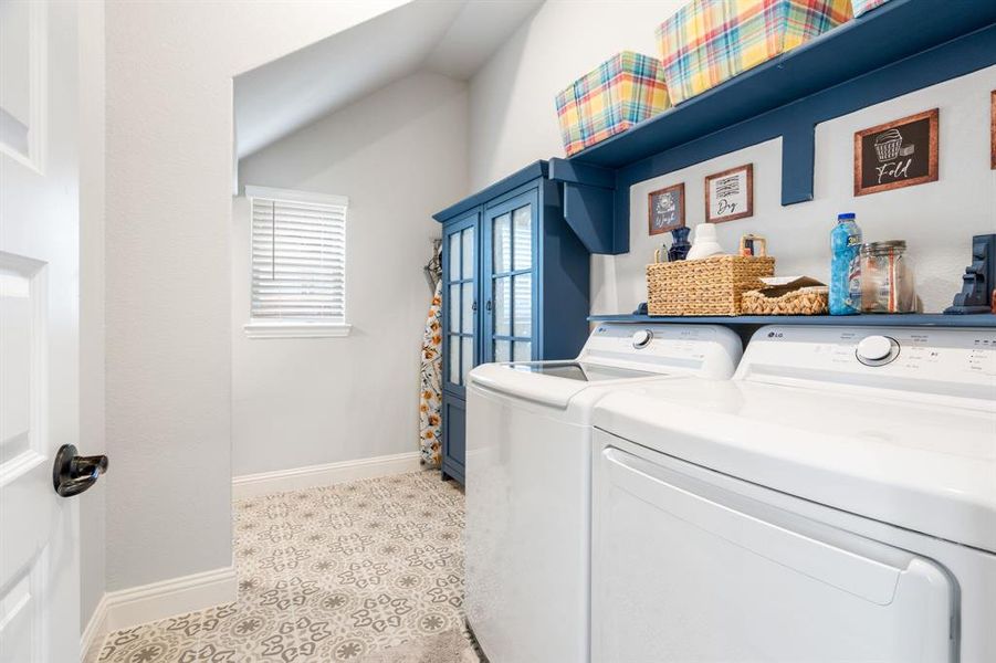 Dedicated laundry space featuring patterned floor tile, a window with blinds, and built-in blue shelving with a lower cabinet Dedicated laundry space featuring patterned floor tile, a window with blinds, and built-in blue shelving with a lower cabinet