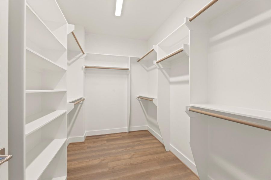 Spacious walk-in closet featuring multiple shelves and hanging rods, with bright lighting and warm flooring for a modern and functional design.