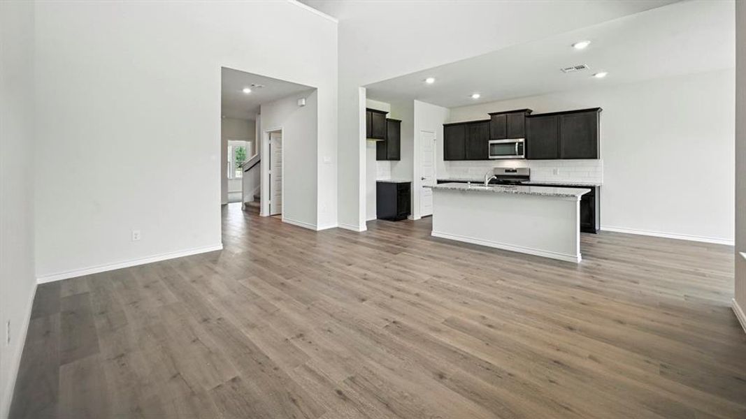 Kitchen with open floor plan, a center island with sink, stainless steel appliances, dark wood-style floors, and recessed lighting