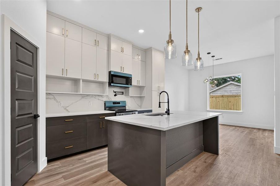 Modern kitchen featuring two-tone cabinetry with gold-tone hardware, a waterfall island with a gooseneck faucet, a patterned backsplash, and wood-finish flooring Modern kitchen featuring two-tone cabinetry with gold-tone hardware, a waterfall island with a gooseneck faucet, a patterned backsplash, and wood-finish flooring