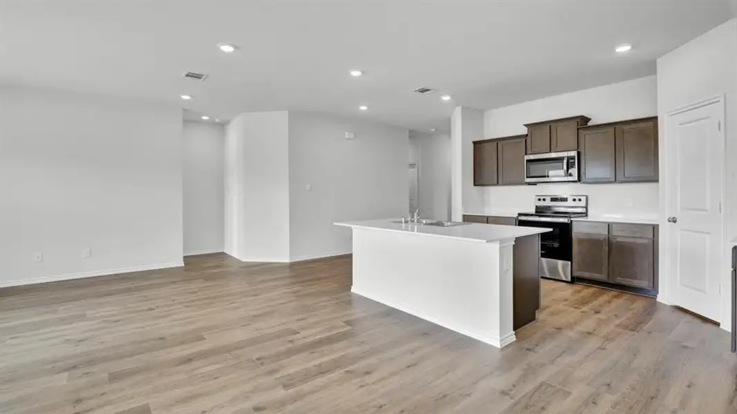 Kitchen featuring light countertops, stainless steel appliances, an island with sink, recessed lighting, and dark wood finish cabinetry