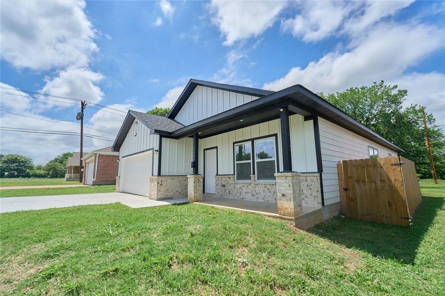 Contemporary-style residence featuring white vertical and horizontal siding, a covered entry porch, a dark shingled roof, stone veneer accents, and an attached garage with a white door