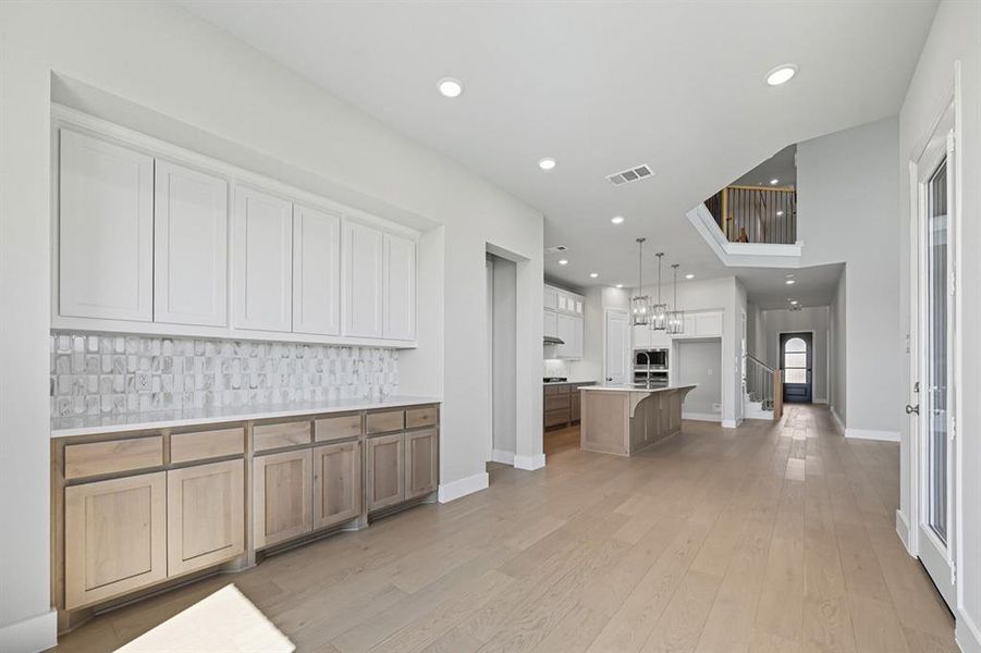 Kitchen with brown cabinets, a kitchen island with sink, decorative backsplash, light wood-style floors, and white cabinets