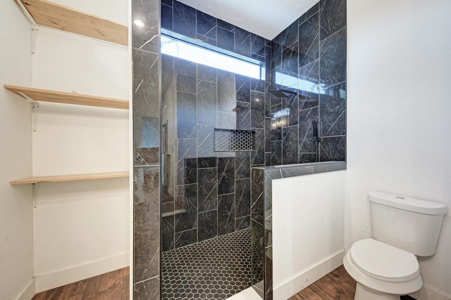 A walk-in tile shower stands adjacent to built-in open shelving and a toilet.