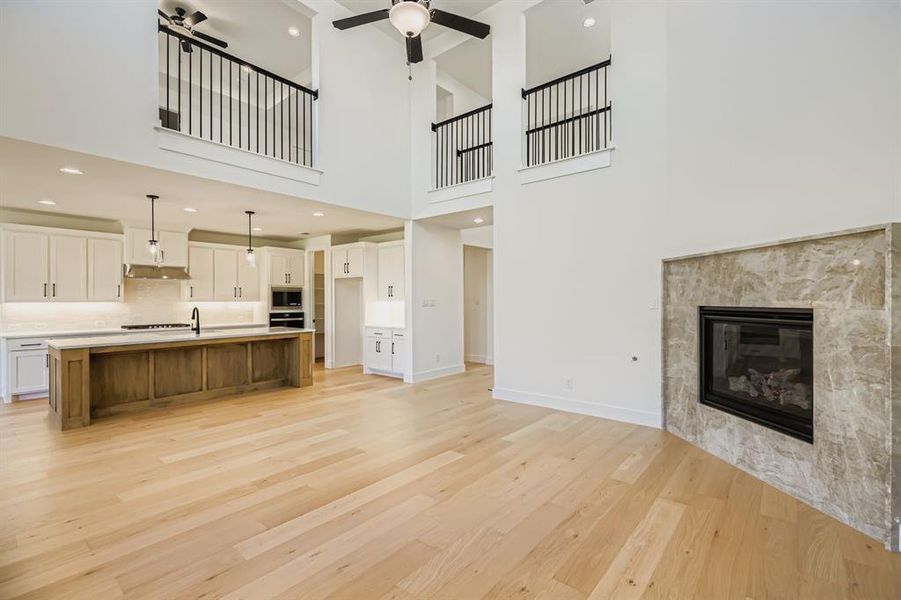 Unfurnished living room with light wood-style flooring, a tile fireplace, a high ceiling, and recessed lighting Unfurnished living room with light wood-style flooring, a tile fireplace, a high ceiling, and recessed lighting