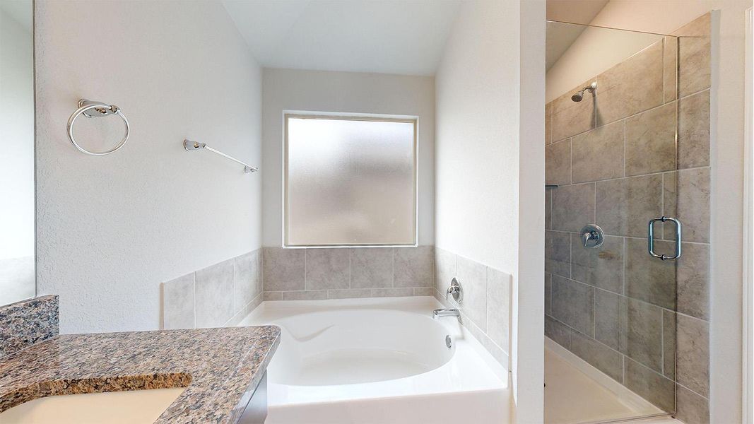 Bathroom featuring a white soaking tub with tiled surround, a frosted window, and a separate glass-enclosed shower with large format tile Bathroom featuring a white soaking tub with tiled surround, a frosted window, and a separate glass-enclosed shower with large format tile