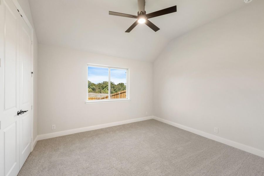 Empty bedroom with vaulted ceiling, ceiling fan, carpet flooring, and a window with backyard view
