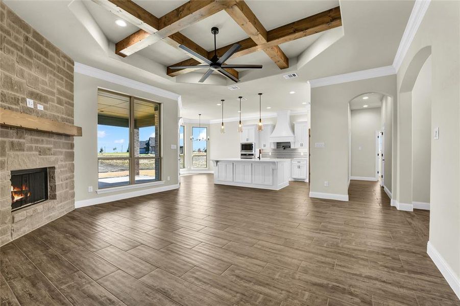 Unfurnished living room with a stone fireplace, beamed ceiling, coffered ceiling, and dark hardwood / wood-style flooring