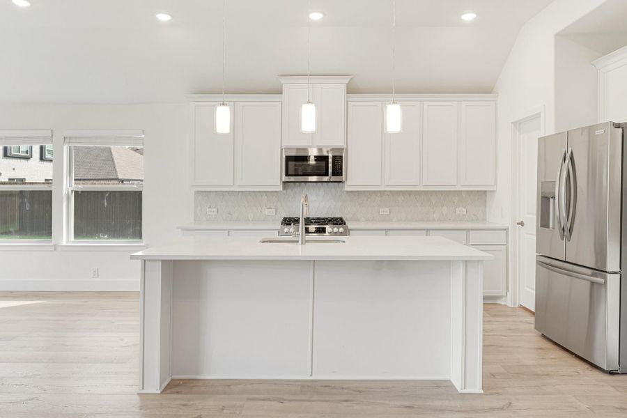 White kitchen with large island, pendant lights, stainless steel appliances, and light hardwood floors