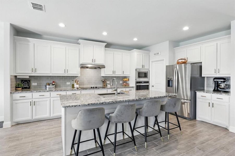 Kitchen with backsplash, stainless steel appliances, recessed lighting, white cabinets, and wood finish floors