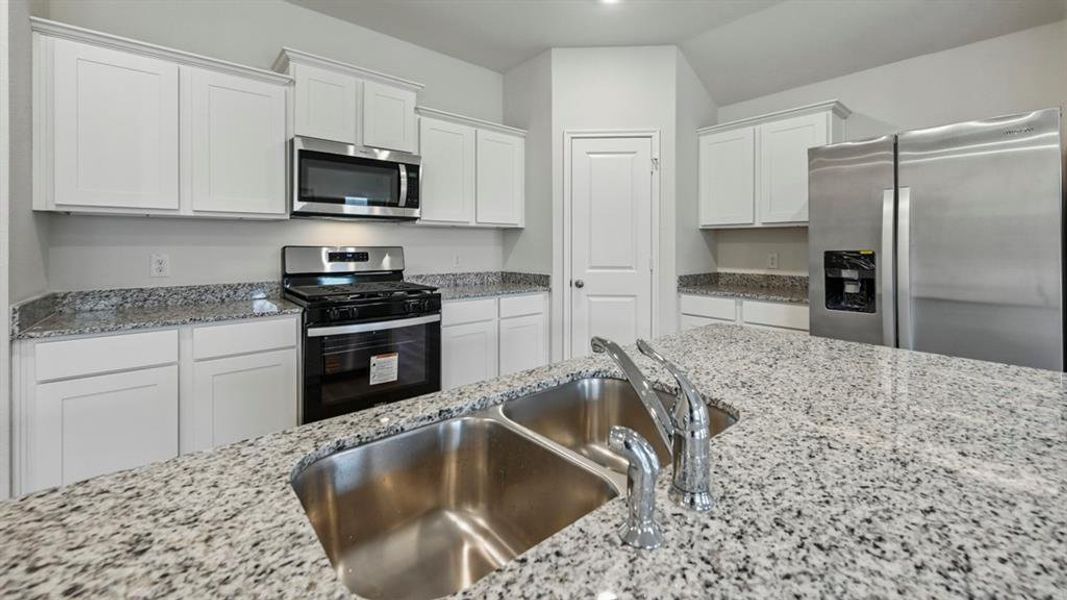 Modern kitchen featuring an island with a double stainless steel sink, granite countertops, white cabinetry, a stainless steel microwave, and a stainless steel range