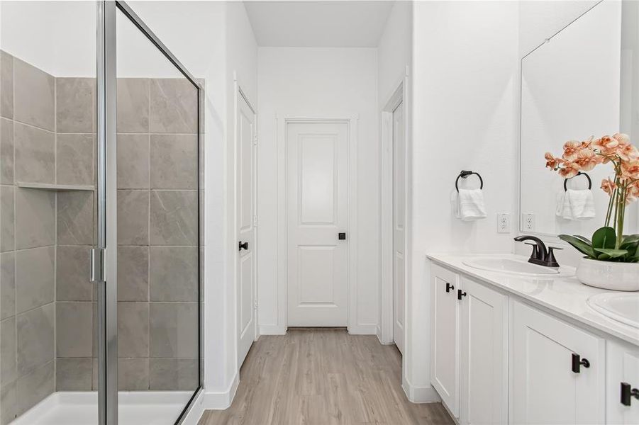 The bathroom features a spacious shower with light gray tile and a glass enclosure, complemented by a white vanity with two sinks and dark hardware