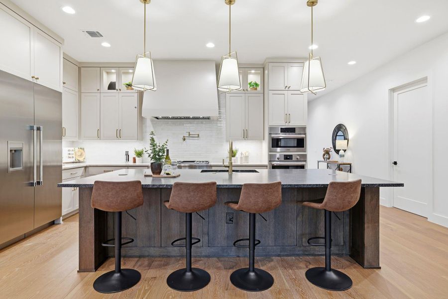 Kitchen with glass insert cabinets, an island with sink, stainless steel appliances, a kitchen bar, and light wood-style flooring