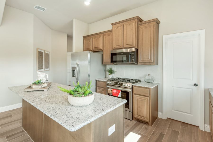 Kitchen with granite island, brown wood cabinets, and stainless steel appliances on wood-look tile floors
