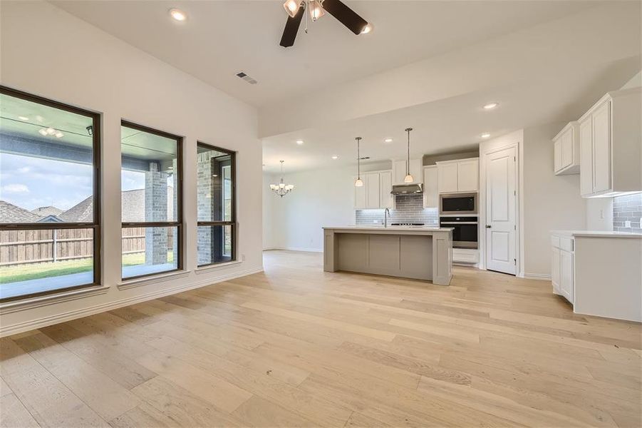 Kitchen with stainless steel appliances, light wood-type flooring, a kitchen island with sink, and backsplash