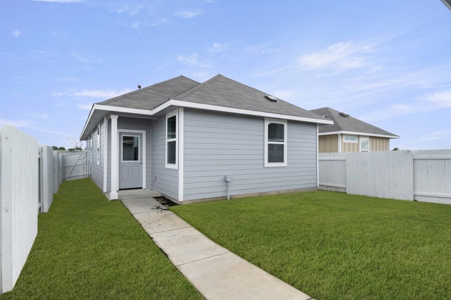 Image of the back exterior of a grey one story home with a back door and concrete pathway