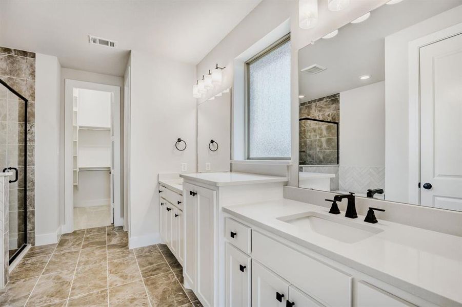 Full bathroom with a shower stall, two vanities, and a walk in closet