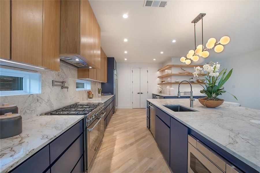 Kitchen with light stone countertops, sink, stainless steel appliances, tasteful backsplash, and decorative light fixtures