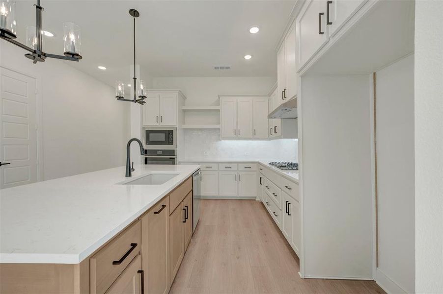 Contemporary kitchen featuring an expansive island with a matte black gooseneck faucet and undermount sink, white quartz countertops, white upper and lower cabinetry, and wood-finish flooring Contemporary kitchen featuring an expansive island with a matte black gooseneck faucet and undermount sink, white quartz countertops, white upper and lower cabinetry, and wood-finish flooring