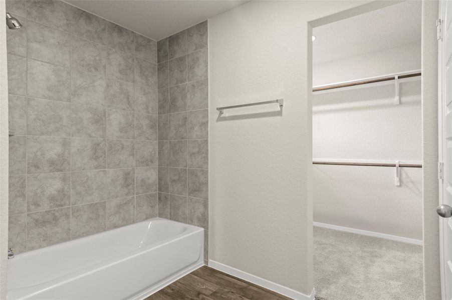 Bathroom with a spacious closet,  shower combination, and wood finished floors