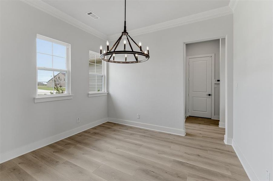 Room featuring wood-finish flooring, two windows with white trim, a contemporary black metal chandelier, and a doorway with a panel door