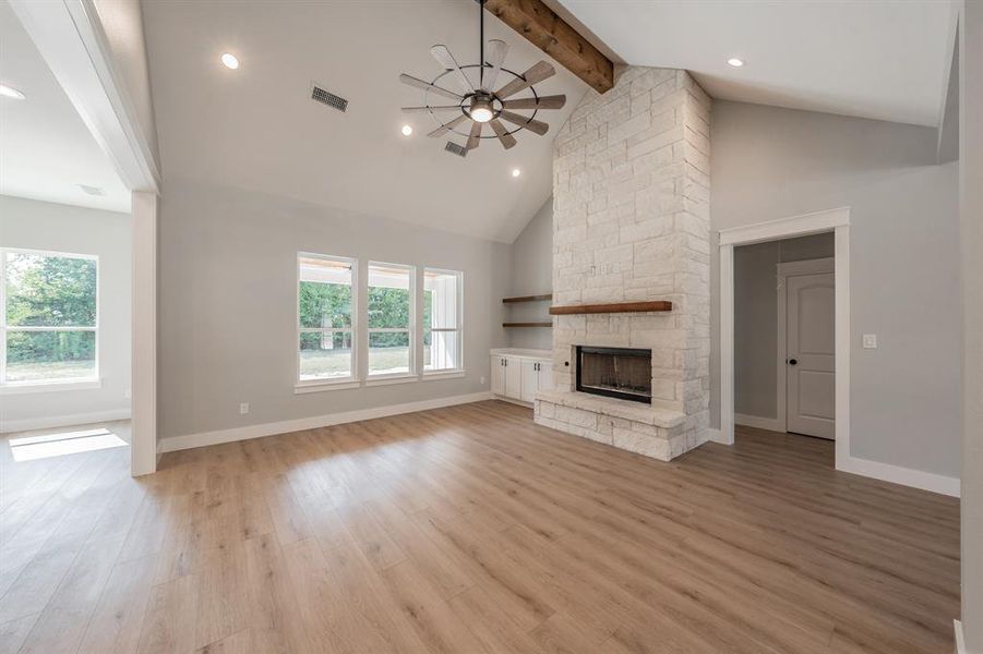 Unfurnished living room featuring ceiling fan, light wood-type flooring, high vaulted ceiling, and a stone fireplace