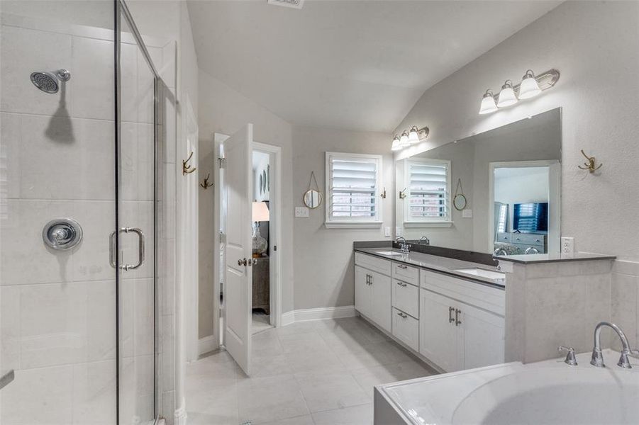 Bathroom with tile floors, double vanity, shower with separate bathtub, and lofted ceiling