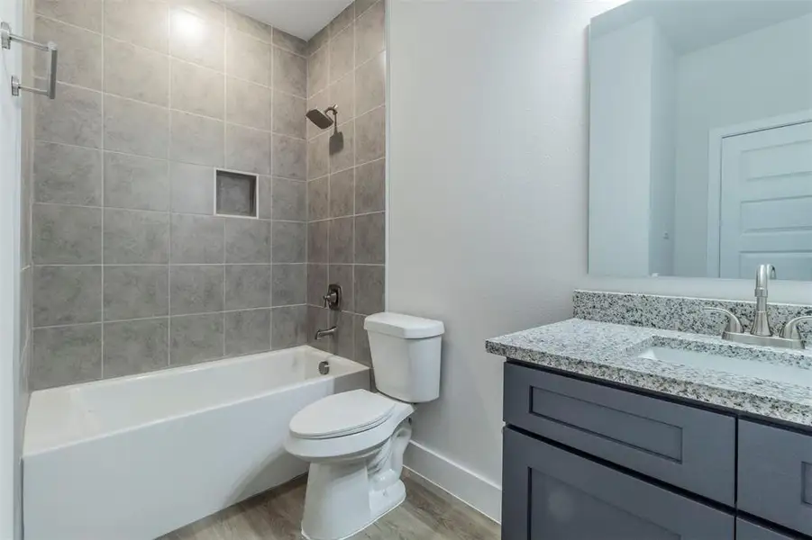 Full bathroom with toilet, hardwood / wood-style flooring, tiled shower / bath combo, and vanity