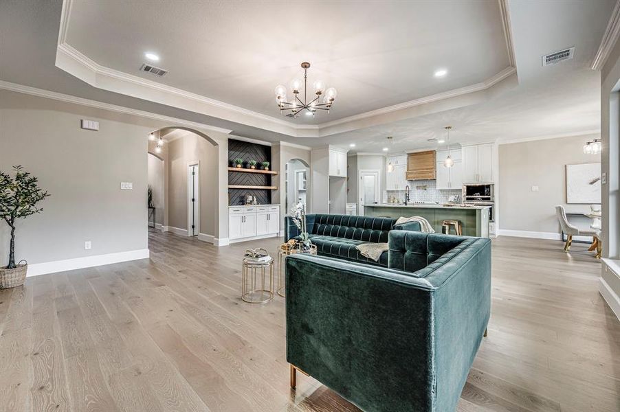 Living room featuring an inviting chandelier, a raised ceiling, and light wood-type flooring