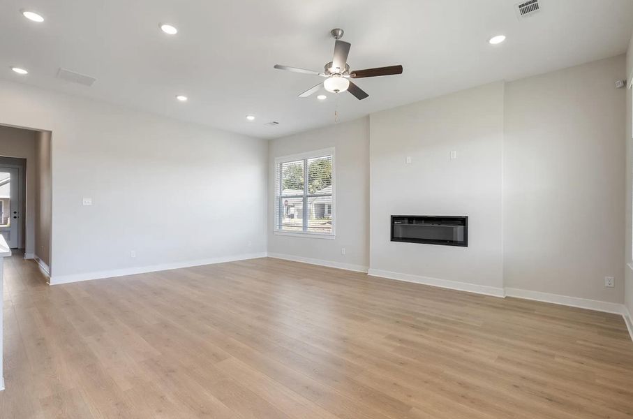 Spacious living area featuring light wood-finish flooring, a contemporary built-in fireplace, and recessed lighting