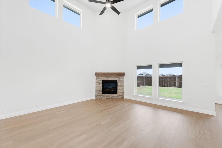 Open living room with two-story ceiling, stone fireplace, hardwood floors, and ceiling fan Open living room with two-story ceiling, stone fireplace, hardwood floors, and ceiling fan