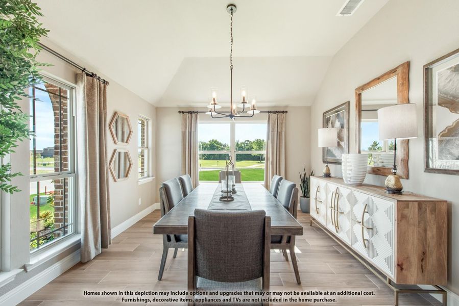 Dining room with long table, gray chairs, chandelier, vaulted ceiling, and large windows with backyard view