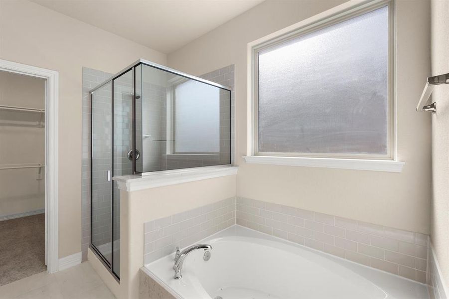 This additional view of your primary bathroom features tile flooring, fresh paint, walk-in shower, a separate garden tub, and a large walk-in closet.