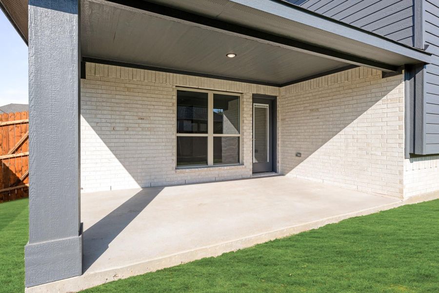 Covered concrete patio with recessed lighting, white brick exterior, and back door entry next to green lawn Covered concrete patio with recessed lighting, white brick exterior, and back door entry next to green lawn