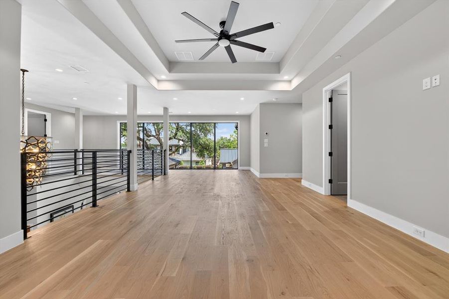 Spacious upper-level area featuring light wood-finish flooring and a tray ceiling with a contemporary ceiling fan Spacious upper-level area featuring light wood-finish flooring and a tray ceiling with a contemporary ceiling fan