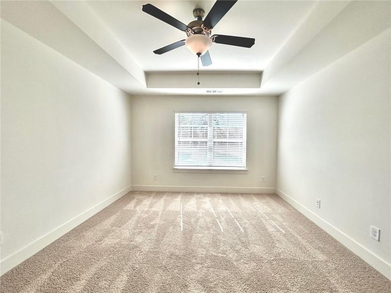 Spare room featuring ceiling fan, a tray ceiling, and light colored carpet