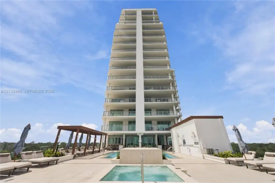 High-rise building exterior featuring tiered balconies with metal railings, elevated terrace level, tiled sundeck, built-in swimming pool, and custom pergola structure