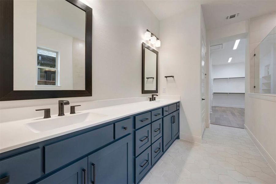 The property features a vanity with dual sinks, a large mirror, and a sophisticated dark blue cabinet with dark hardware