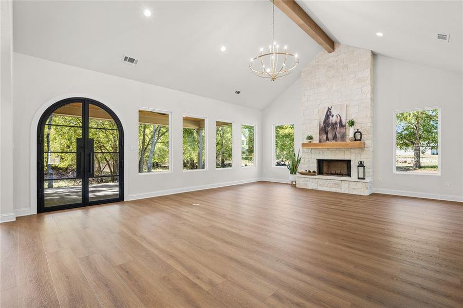 Unfurnished living room with high vaulted ceiling, beamed ceiling, plenty of natural light, light wood-type flooring, and a fireplace