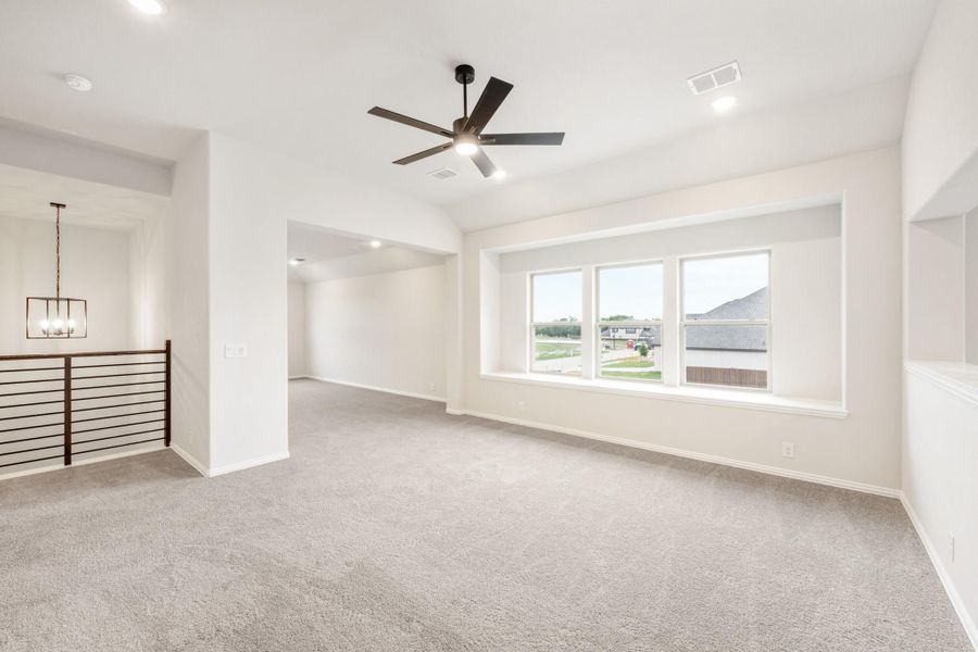 Open living area with gray carpet, ceiling fan, large windows, and staircase railing visible Open living area with gray carpet, ceiling fan, large windows, and staircase railing visible