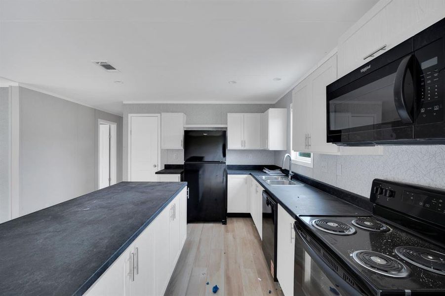 Kitchen with black appliances, dark countertops, white cabinetry, light wood-style flooring, and ornamental molding