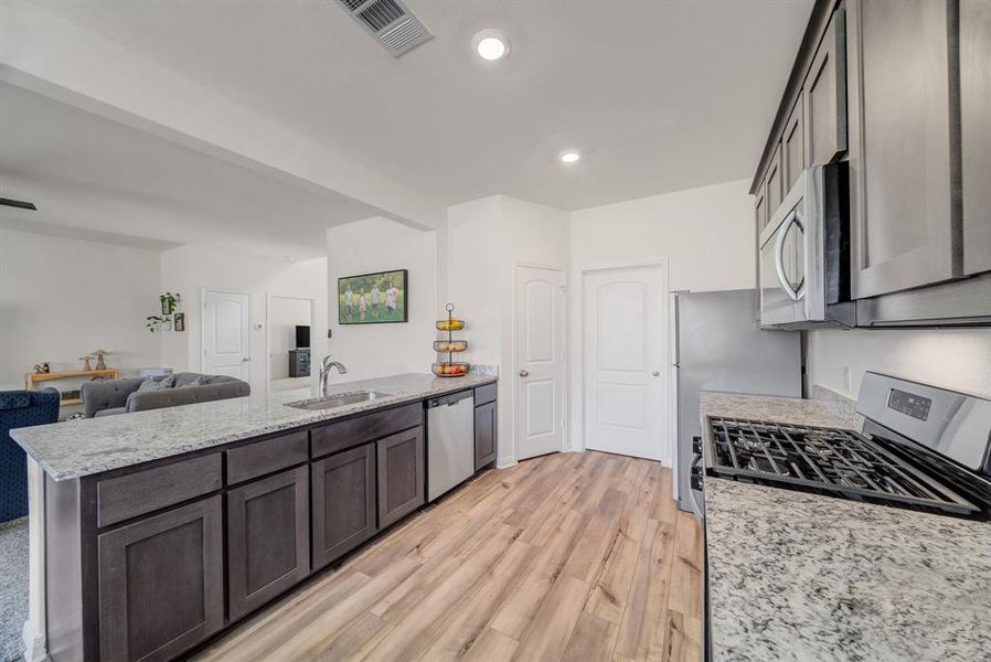 Kitchen featuring light stone countertops, a peninsula, light wood-style flooring, appliances with stainless steel finishes, and recessed lighting